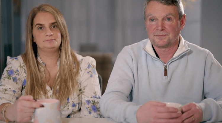 A woman and a man sit at a table, each holding a mug.