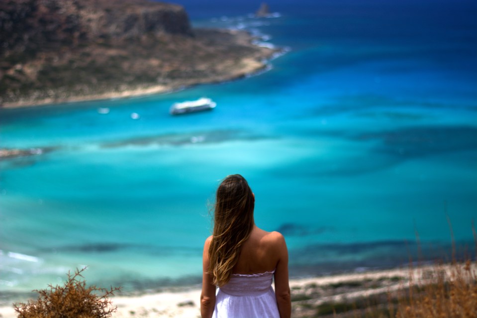 Woman in white dress overlooking turquoise ocean.