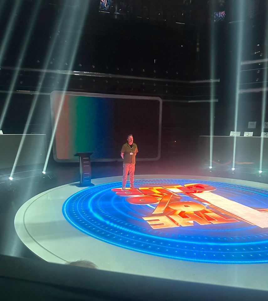 A man stands on a stage with the words "The 1% Club" illuminated on the floor.