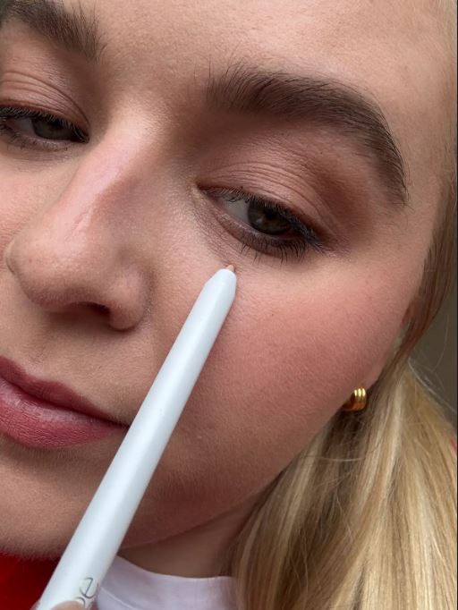 Close-up of a person applying makeup near their eye with a white pencil.