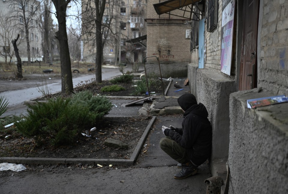 A teenager sits hunched over near a damaged building.