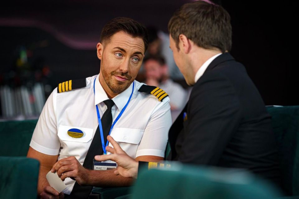 Colin Smallwood, in a pilot's uniform, speaks with Piers in a theater.