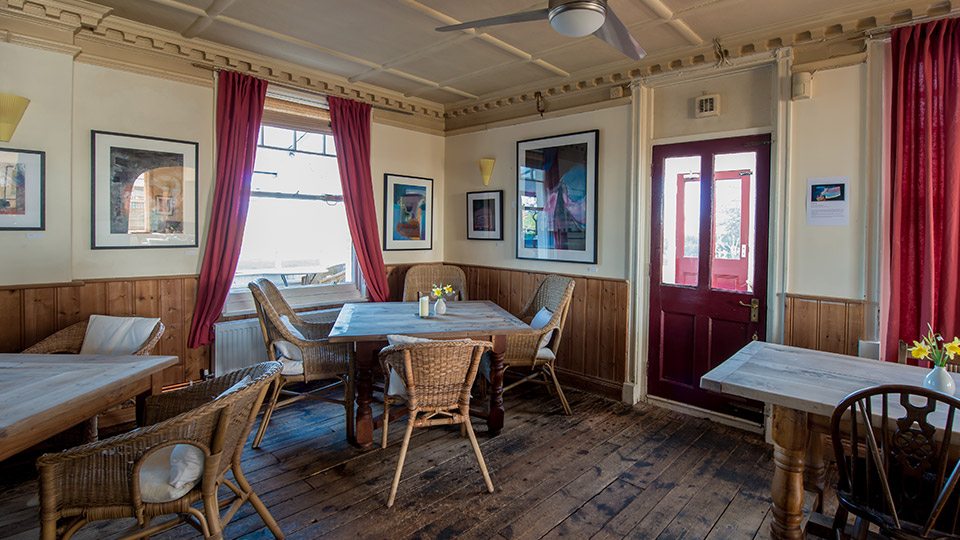 Interior view of a restaurant with wooden floors, wicker chairs, and artwork on the walls.