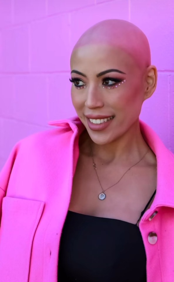 Portrait of a bald woman wearing a pink jacket and sparkly makeup.