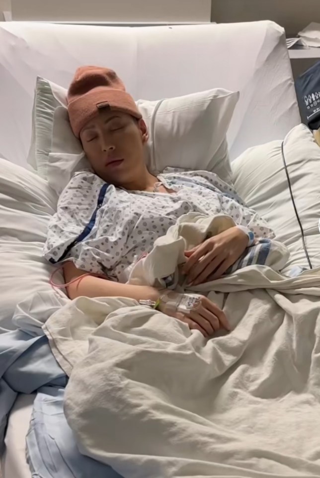 Woman sleeping in a hospital bed wearing a beanie.