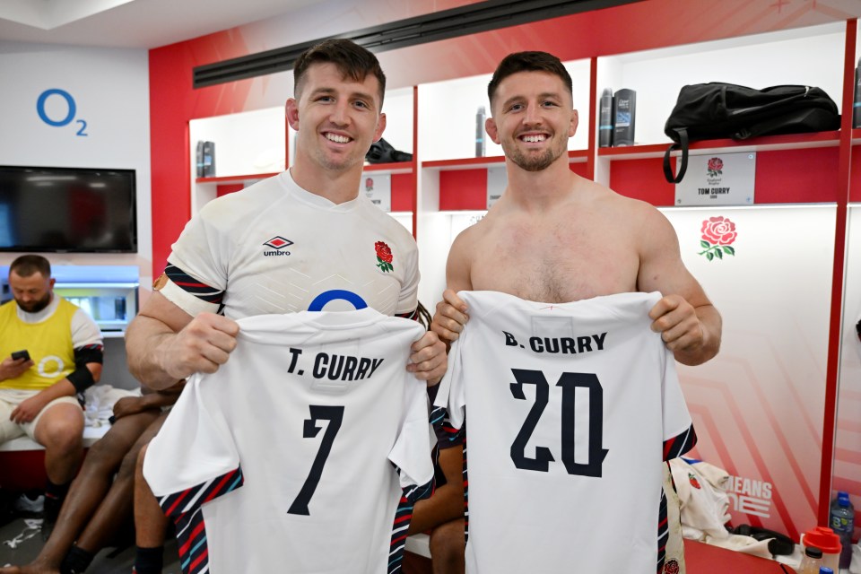 Tom Curry and Ben Curry of England's rugby team holding up their jerseys in a locker room.