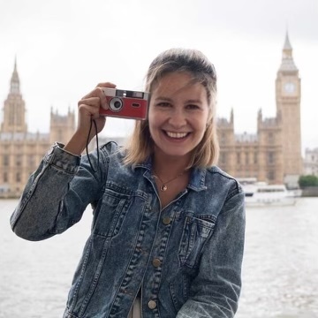 Woman holding a red camera in front of the Houses of Parliament.