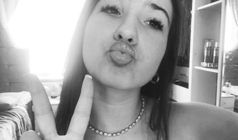 Black and white photo of a young woman making a peace sign and puckering her lips.