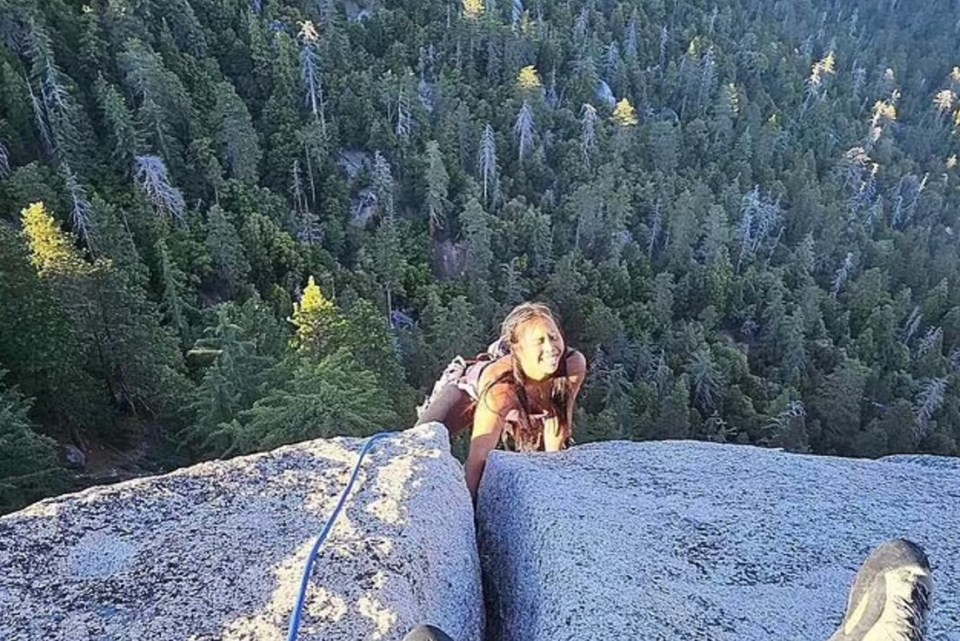 A rock climber perched on a cliff edge overlooking a forest.