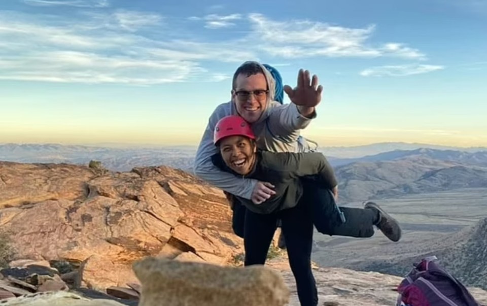 A rock climber piggybacking a friend atop a mountain.