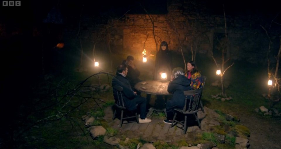 The Traitors contestants gathered around a table at night.