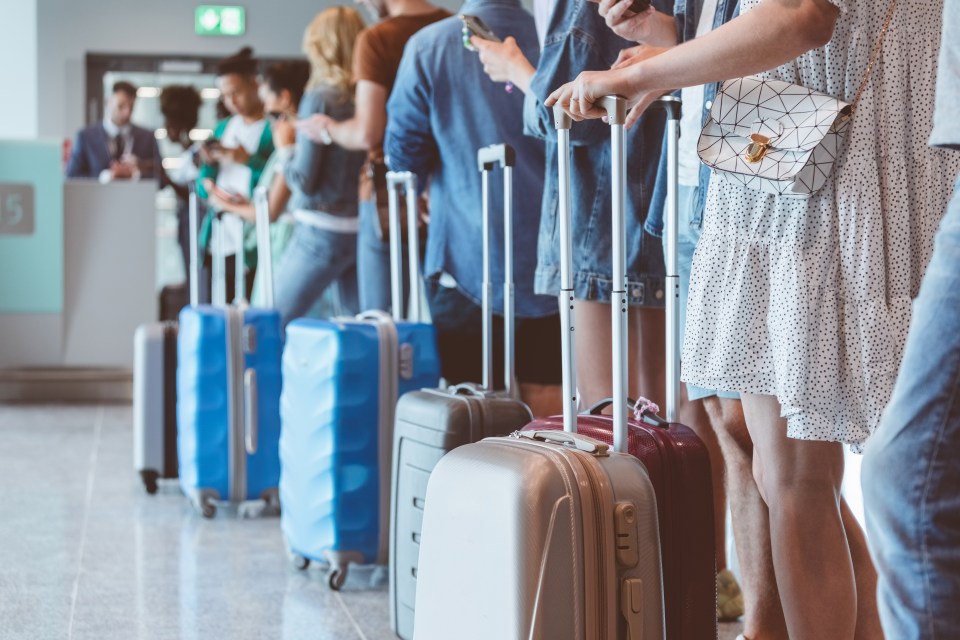 Travelers with luggage using smartphones at an airport check-in.