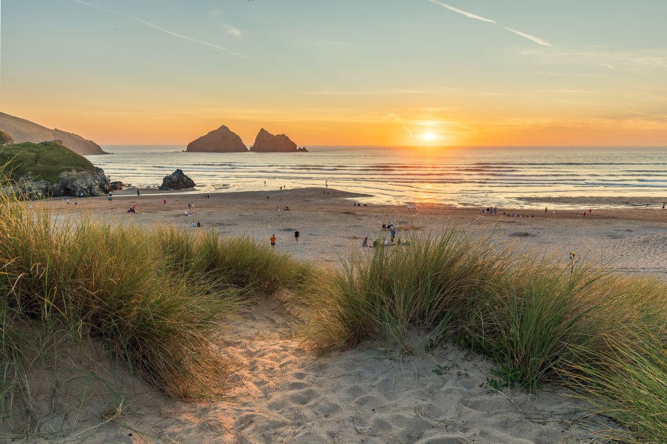 Sunset over Holywell Bay beach in Cornwall, with people relaxing on the sand.