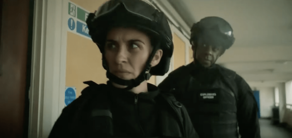 Two police officers in helmets and tactical gear walk down a hallway.