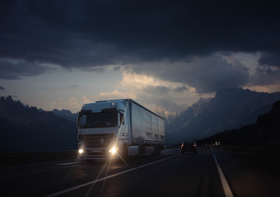 Semi-truck transporting goods on a highway at dusk, mountains in the background.