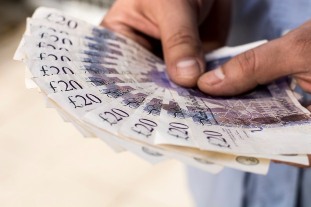 A man's hands holding a fan of twenty-pound British banknotes.