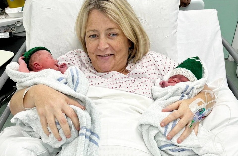 A mother holding her newborn twin babies in a hospital bed.