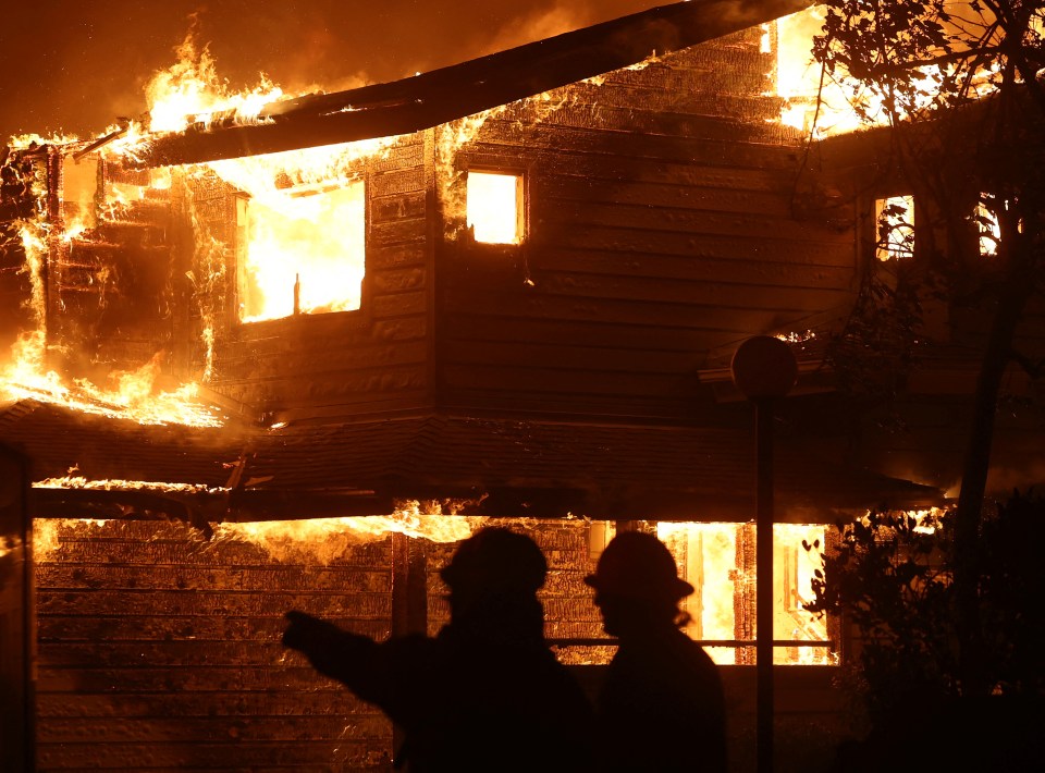 Two firefighters silhouetted against a burning house.