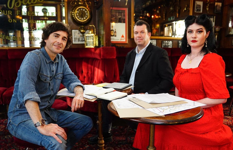 Three people sitting around a table in a pub, reviewing documents.