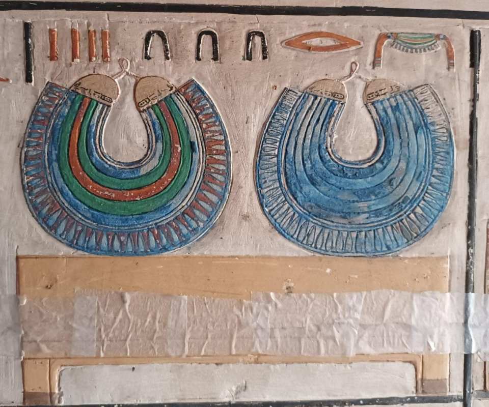 Colorful reliefs depicting ancient Egyptian jewelry on a mastaba wall.