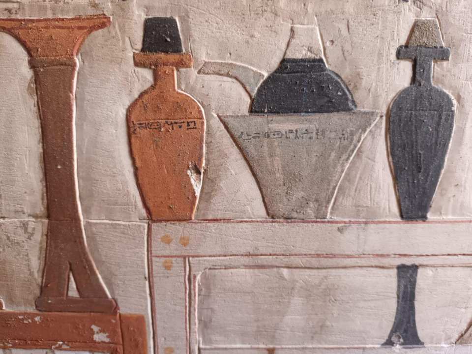 Colorful reliefs of ancient vessels and furniture on a mastaba wall.