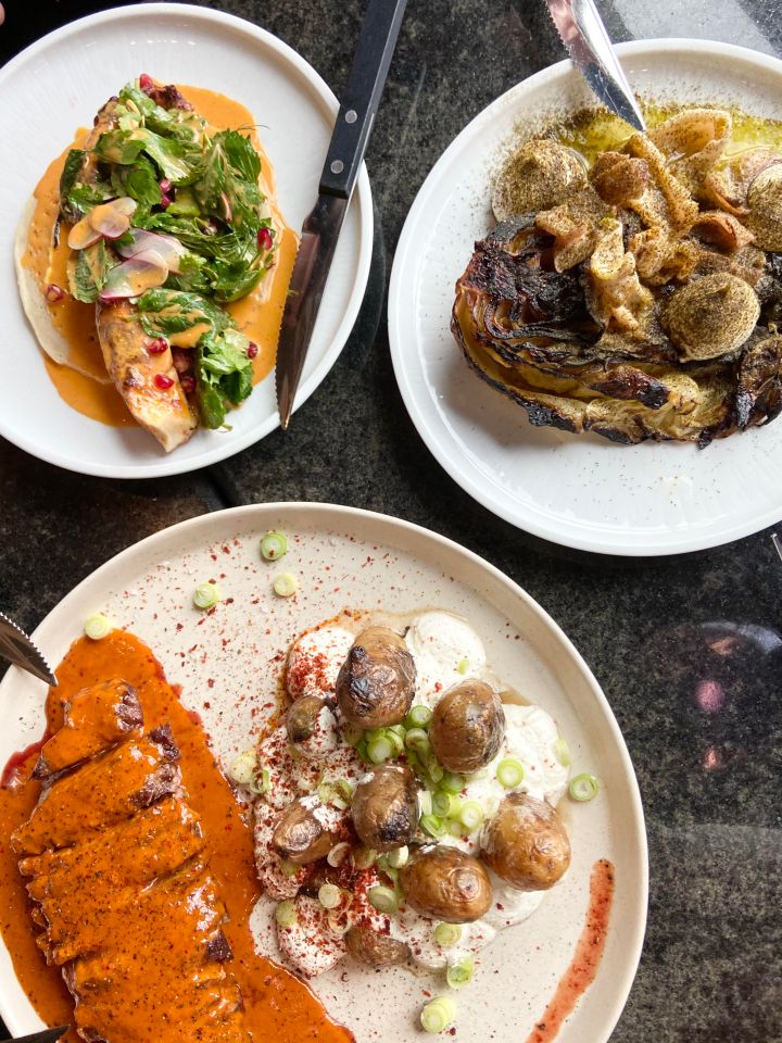 Three plates of food: one with grilled chicken and greens, one with roasted cabbage, and one with sliced meat in a sauce and roasted potatoes.