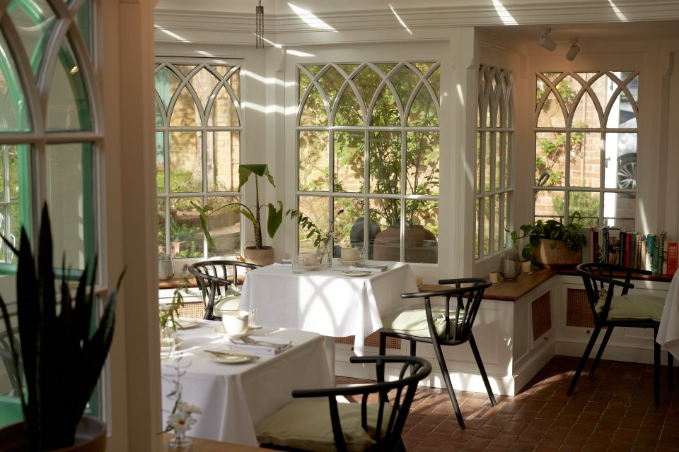 Sunlit dining room with white tablecloths and black chairs.