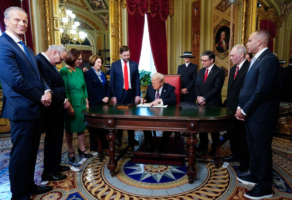 President Trump signing a document at a ceremony, surrounded by government officials.