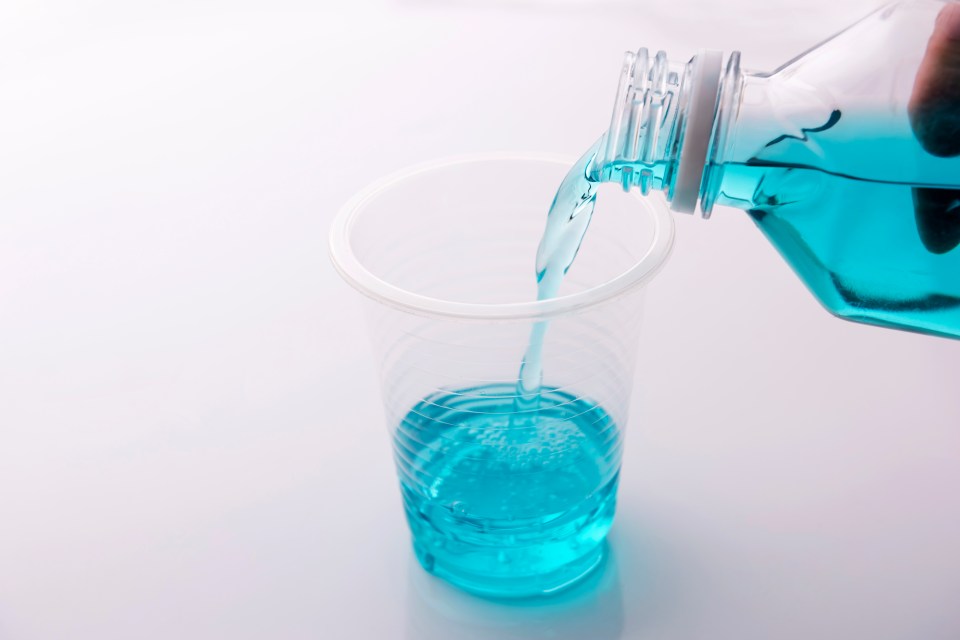 Pouring blue mouthwash into a plastic cup.