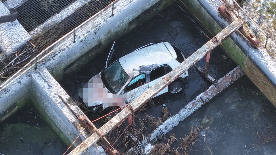 A white car submerged in a sewage pit.