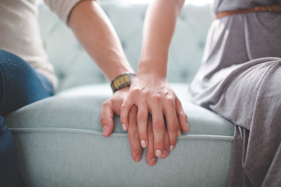 Close-up of a couple holding hands on a couch.