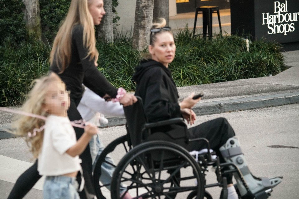 Anna Kournikova in a wheelchair with a leg brace, walking with her family.