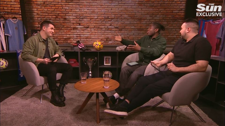 Three men sitting in chairs and discussing soccer.