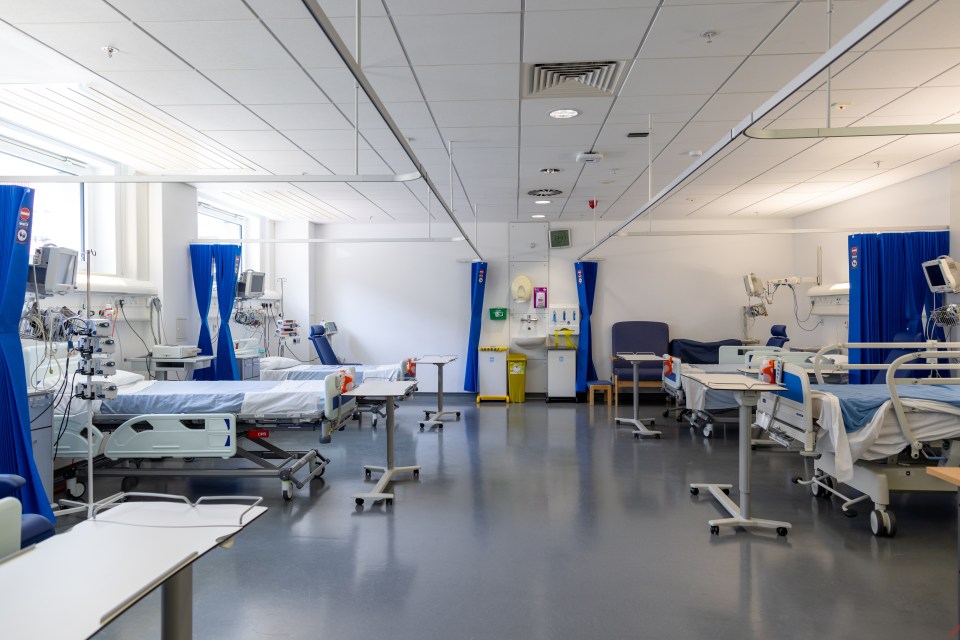 Empty hospital ward with several beds and medical equipment.