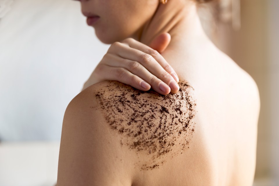 Woman applying coffee scrub to her shoulder.