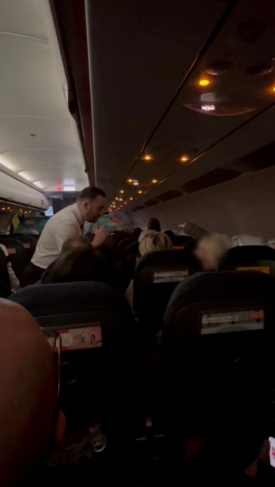 A flight attendant subdues a disruptive passenger on a plane.