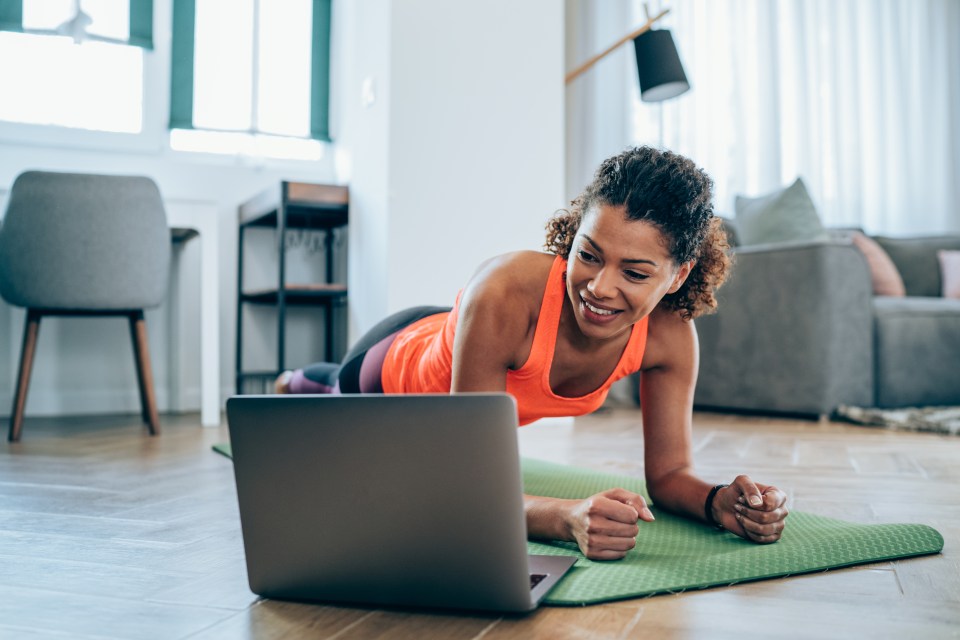 Woman doing a plank exercise while following a workout video on her laptop.