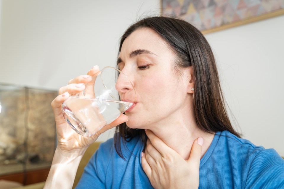 Woman drinking water and holding her throat.