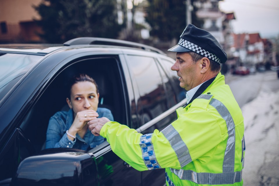 Police officer administering a breathalyzer test to a woman in her car.