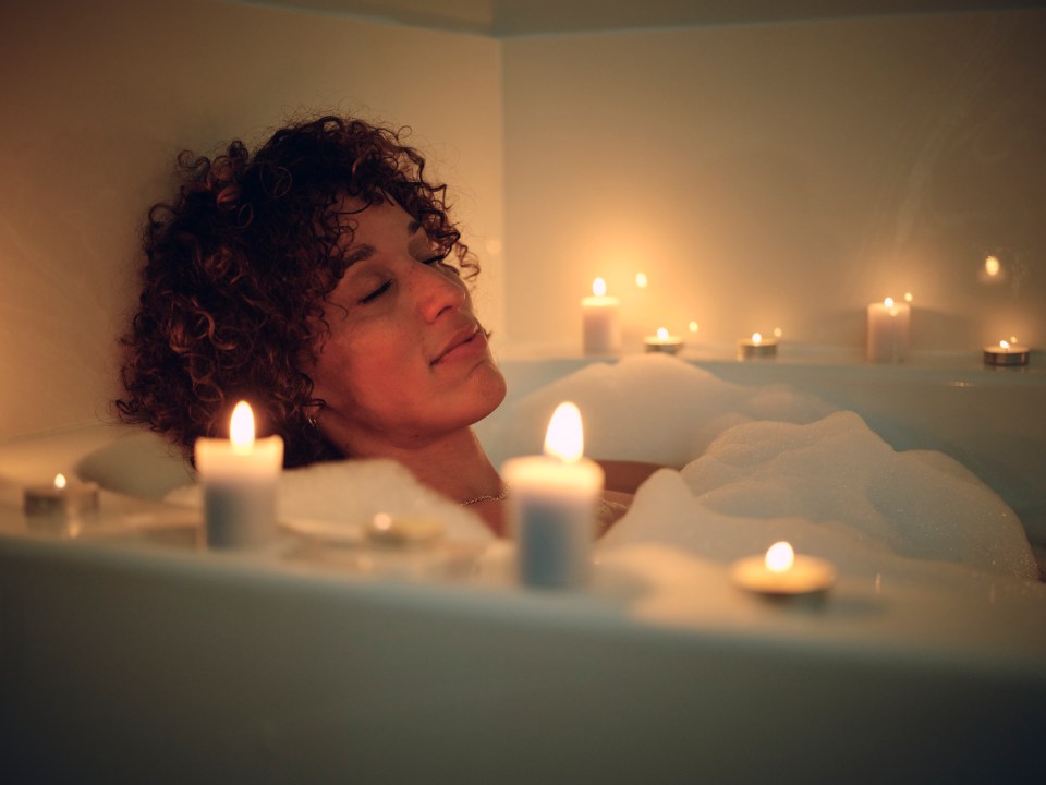 Woman relaxing in a bubble bath surrounded by candles.