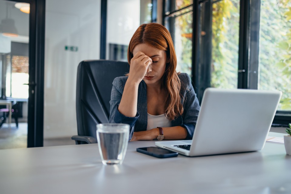 Stressed businesswoman at her desk working on a laptop.