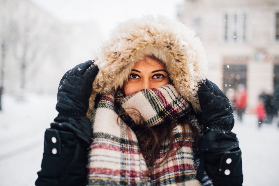 A young woman smiles while bundled in warm winter clothing in the snow.