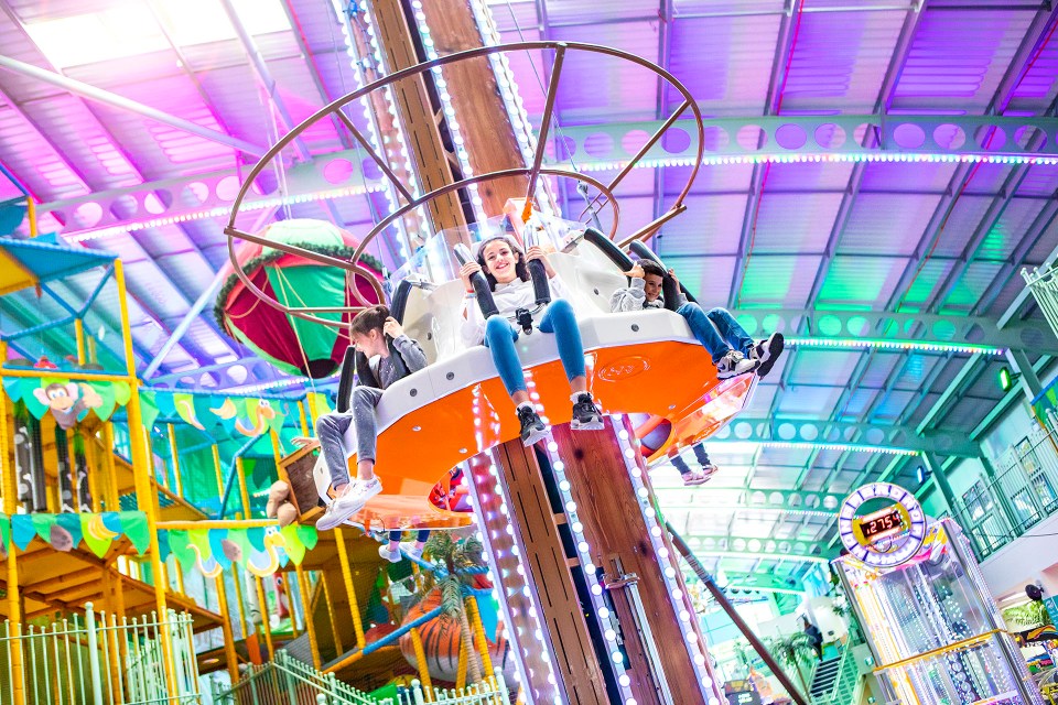 Three children enjoying a ride at an indoor amusement park.