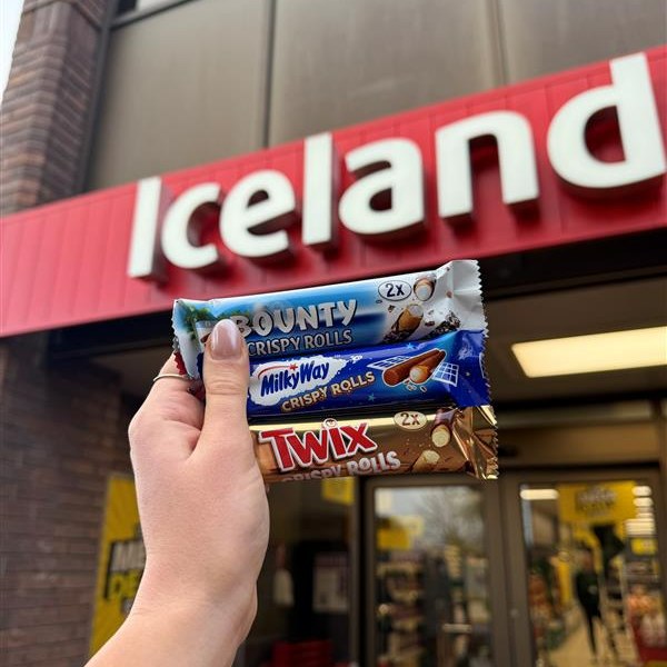 Hand holding three candy bars in front of an Iceland store.