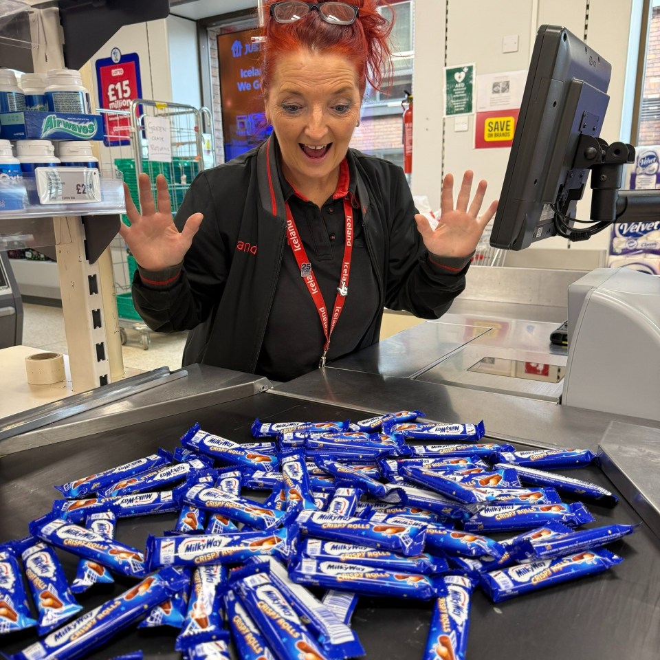 A cashier looks surprised at a large pile of Milky Way Crispy Rolls on a checkout conveyor belt.