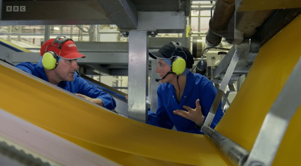 Two workers wearing headsets inspect a large sheet of yellow material on a factory production line.