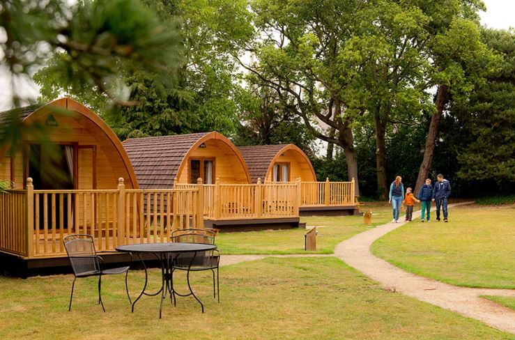 Three glamping pods and a family walking on a path.