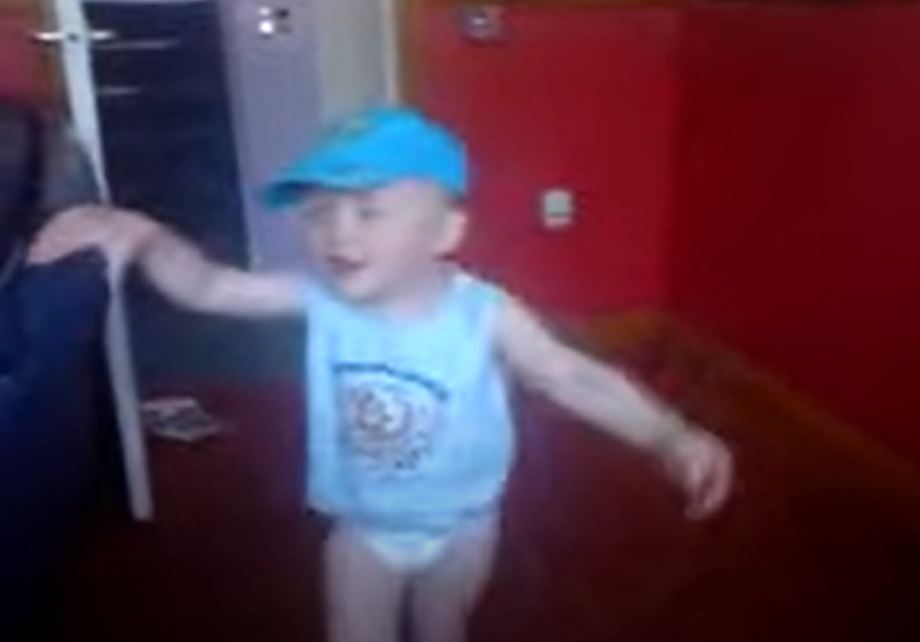 Young boy in a blue cap and shirt dancing.