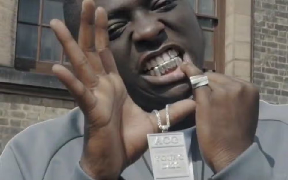 Close-up of a man showing off gold teeth and a silver necklace.