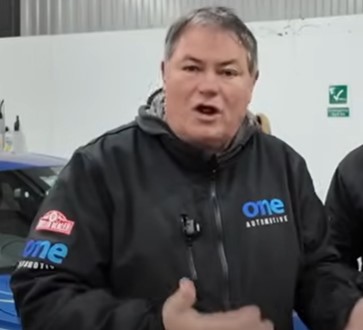 Mike Brewer speaking in a garage.